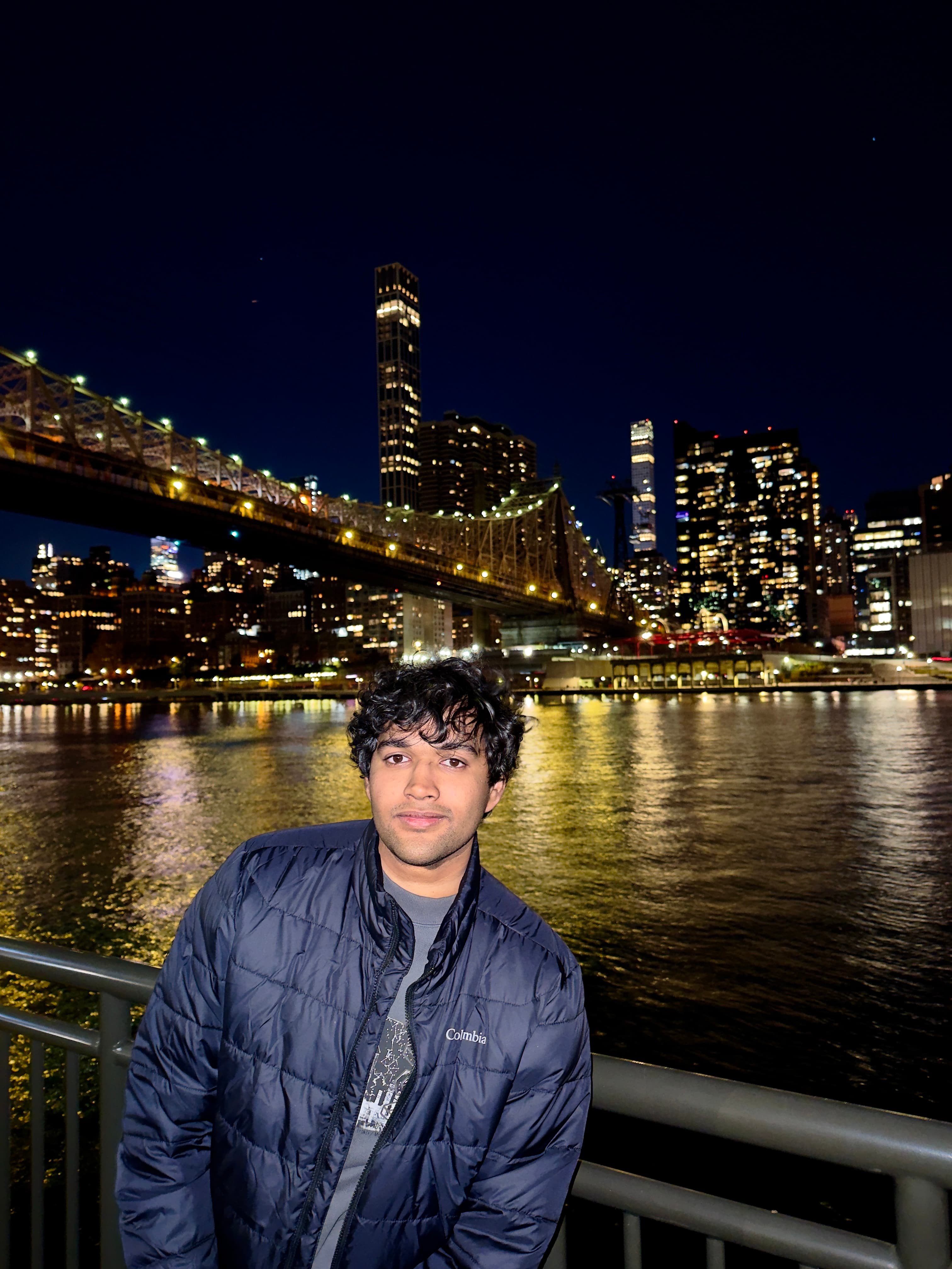 Aayush in New York City at night with the lit-up skyline behind him