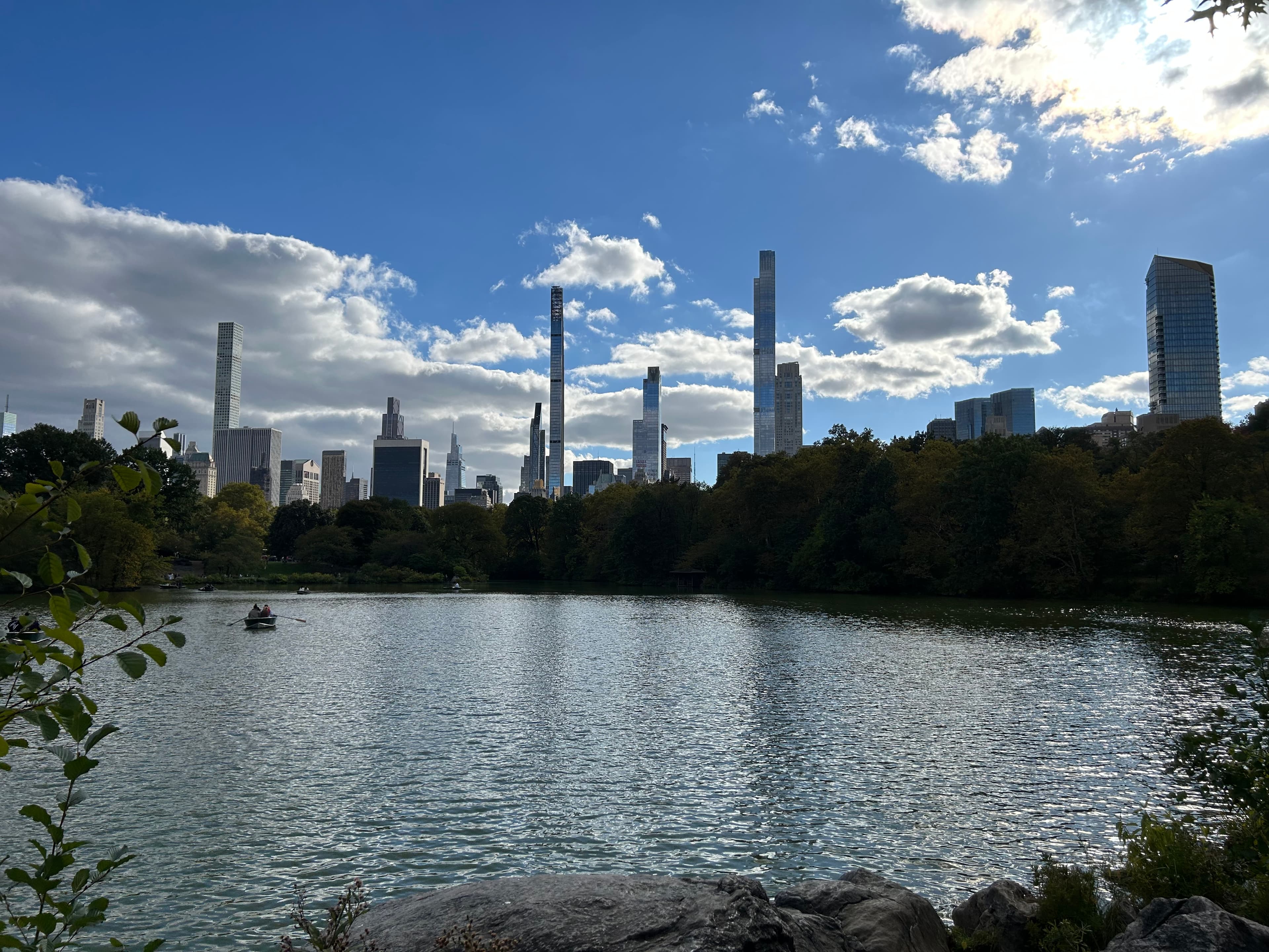 Central Park lake with Billionaires' Row skyscrapers rising above the treeline on a clear day