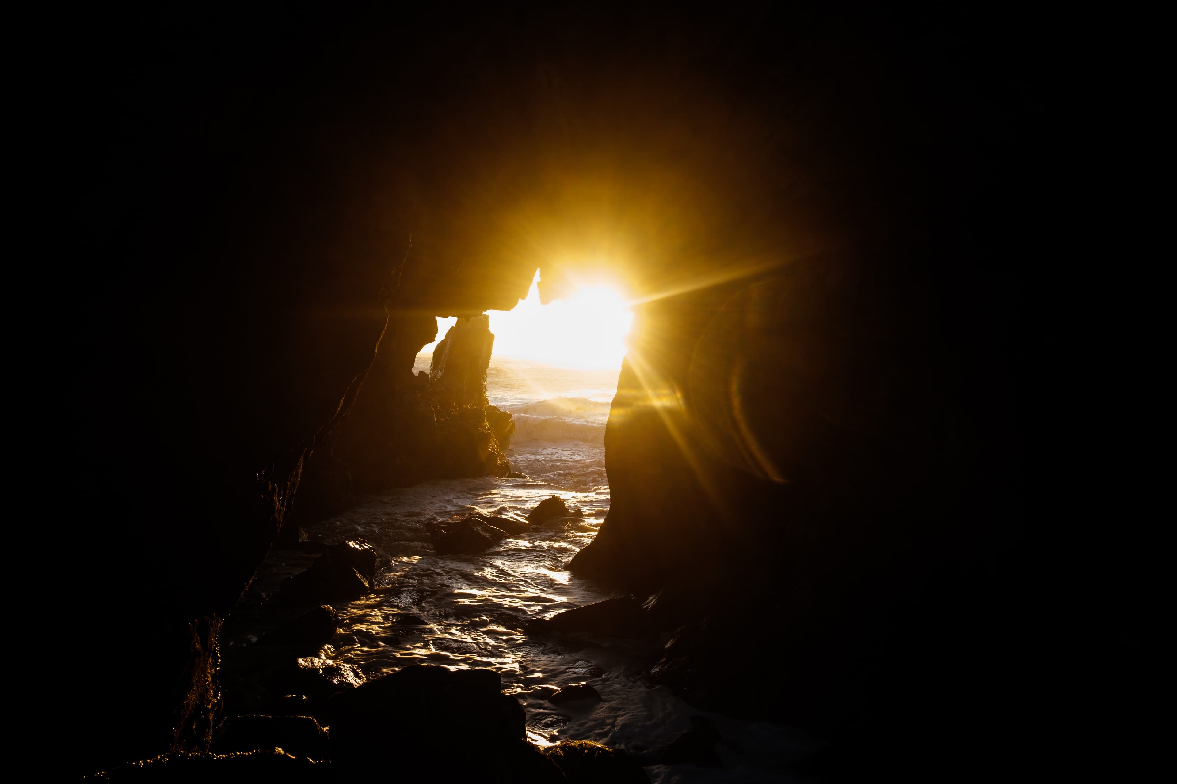 Golden sunburst through a sea cave arch at El Matador Beach