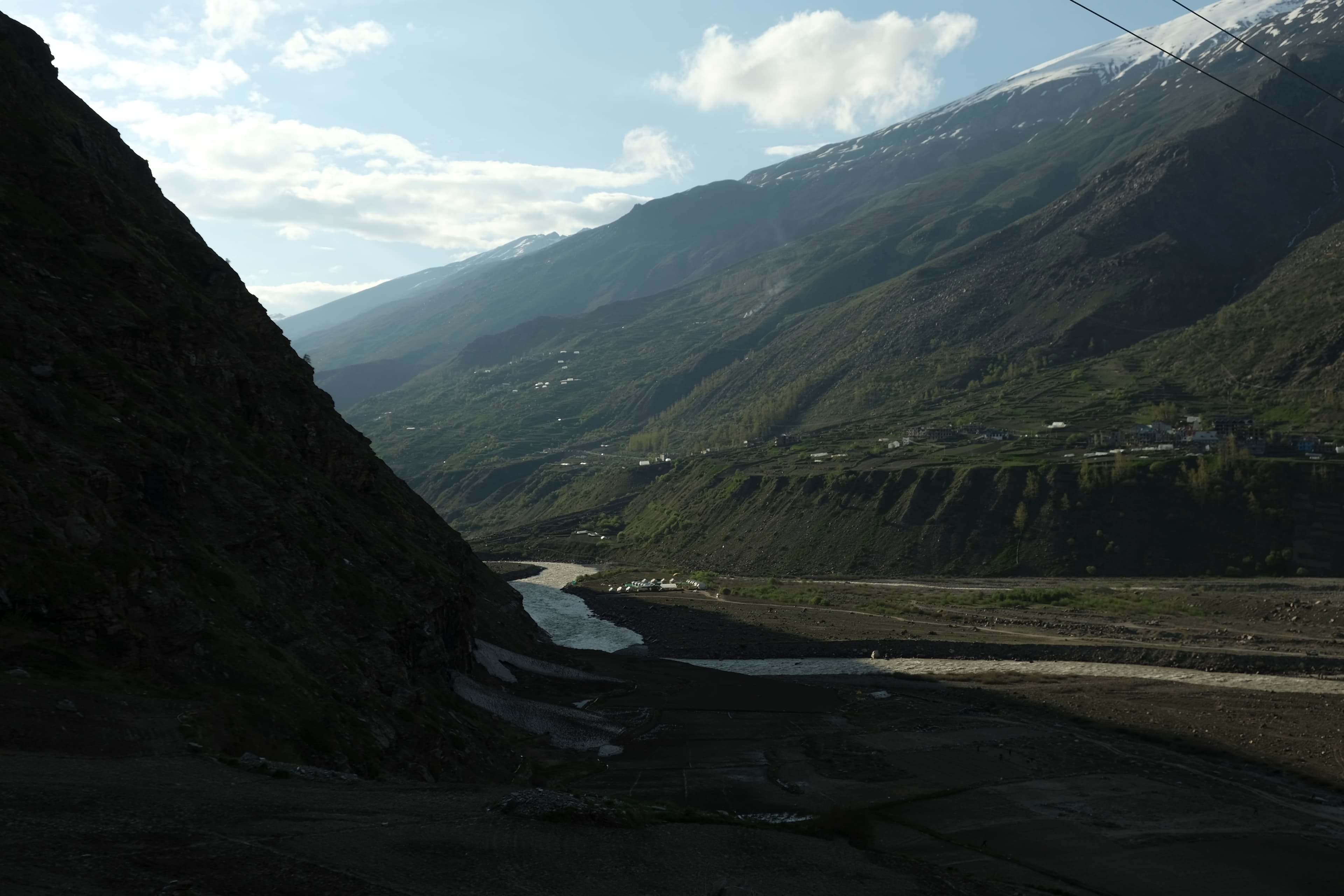 River winding through a Himalayan valley framed by a dark cliff face and snow-capped peaks