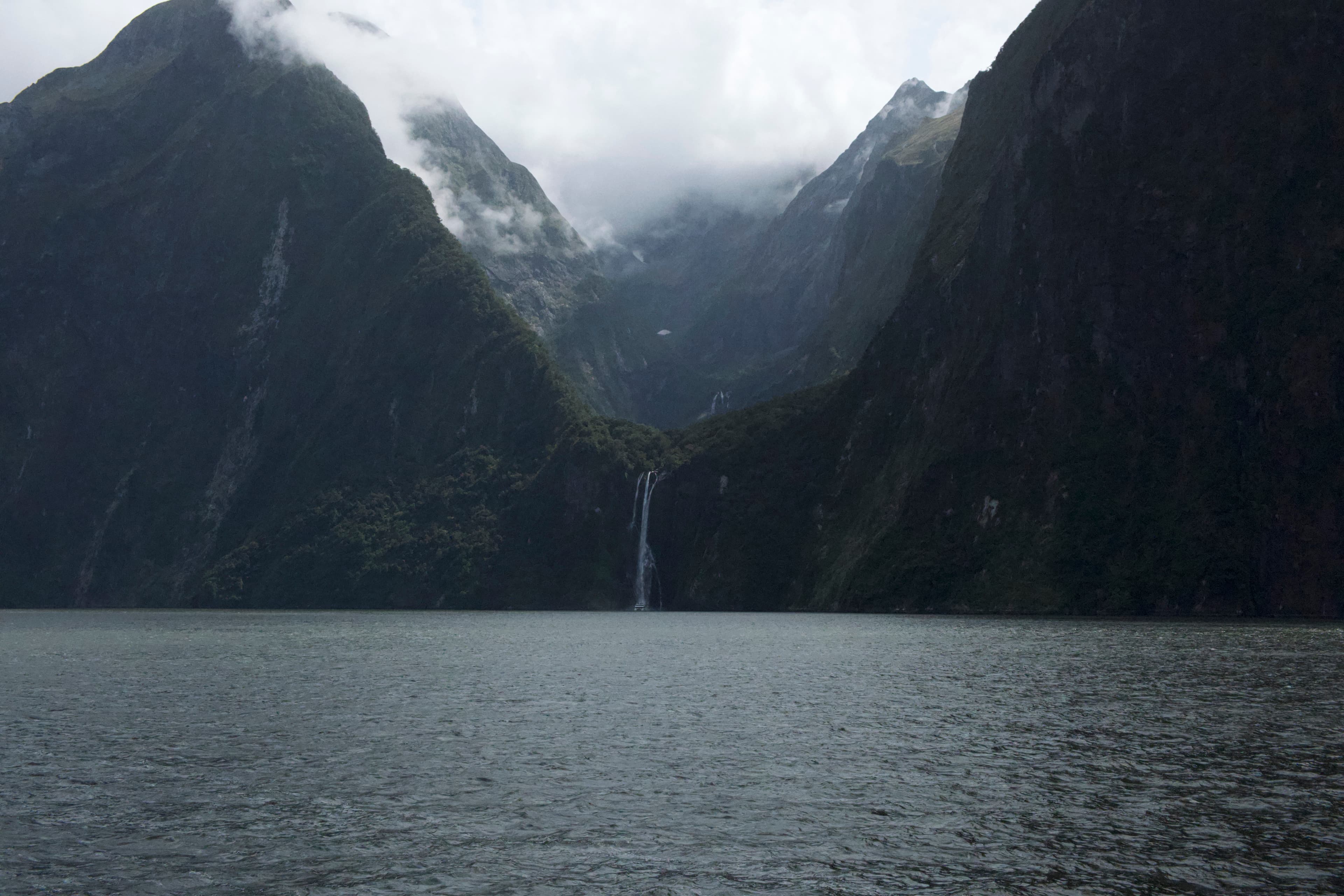 Waterfall cascading into Milford Sound surrounded by sheer cliffs