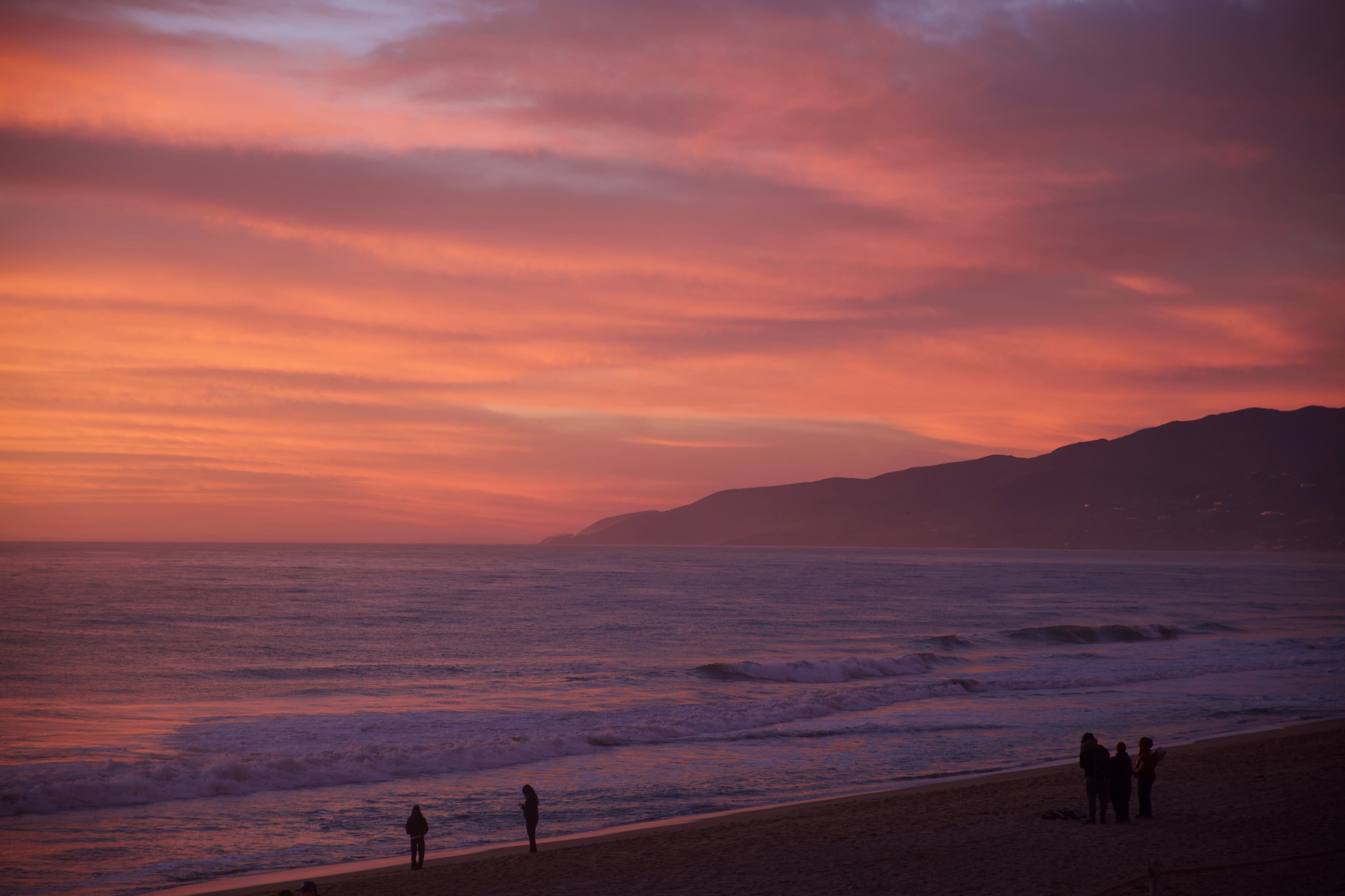 Deep red and pink sunset over the Pacific at Zuma Beach, silhouetted figures on the shore